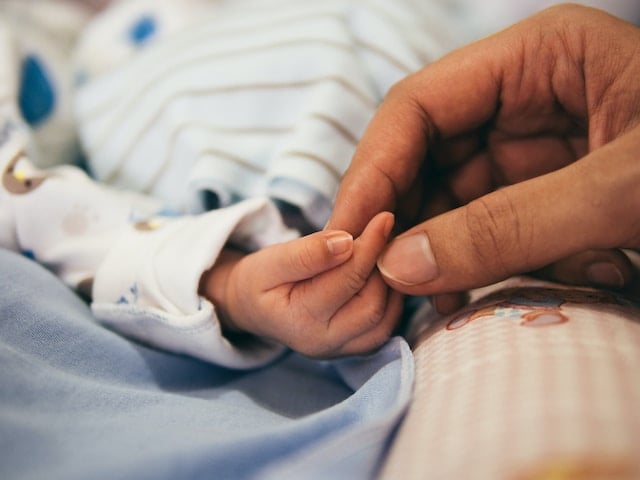An infant holding the finger of a person