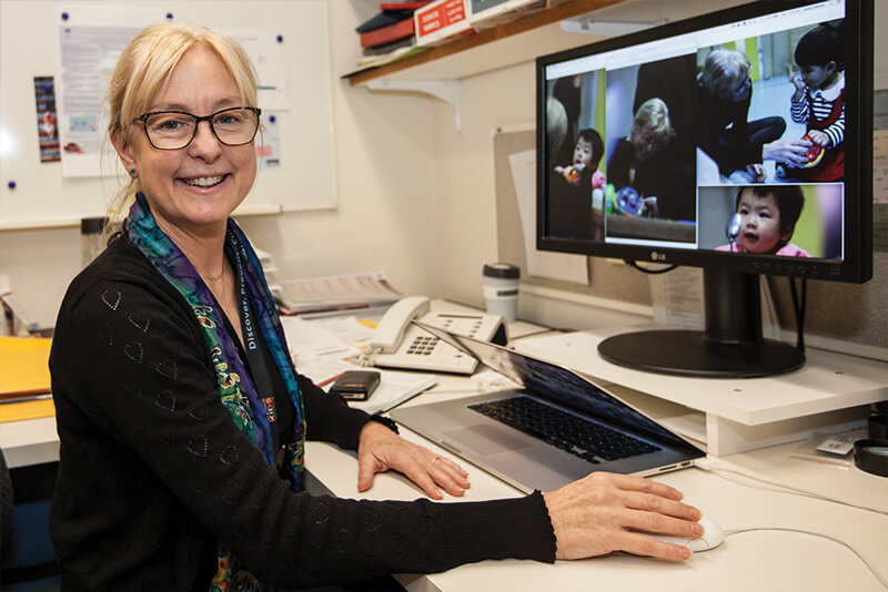 Dr Jenny Downs sitting in front of her computer showing photos of study participants